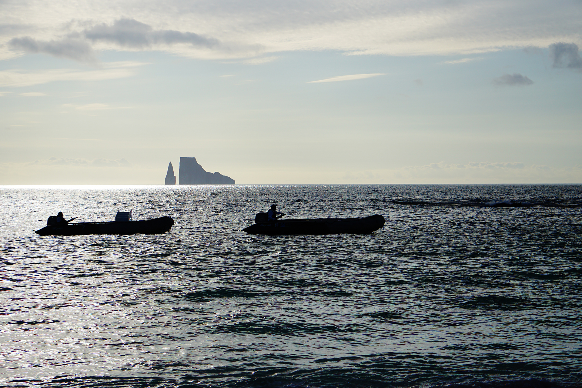 Galápagos&#039; famous Kicker Rock and two Zodiac boats are silhouetted in some dramatic lighting as the sun went behind some clouds in this view from a beach on San Cristóbal.